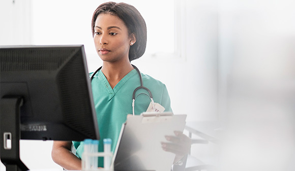 Female nurse wearing mask using laptop while working on medical reports pandemic